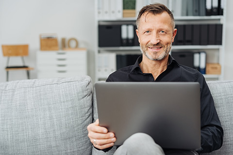 Mann sitzt auf dem Sofa mit Laptop auf dem Schoß.