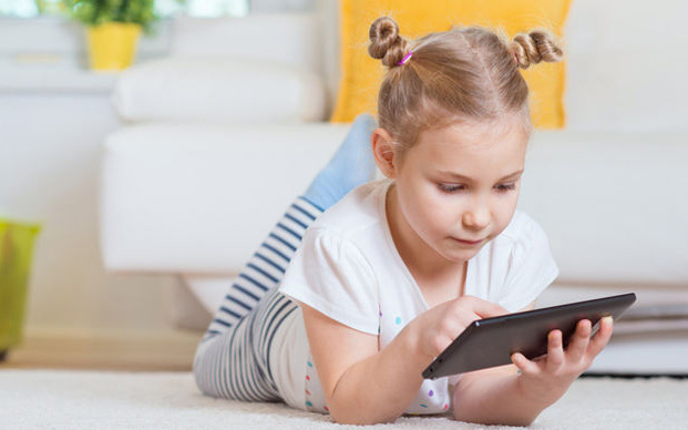 Kleines Mädchen liegt auf dem Bauch mit einem Tablet in den Händen