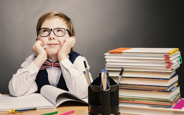 Kleiner Junge mit Brille, Hemd, Weste und Fliege sitzt am Schreibtisch. Den Kopf in die Hände gestützt und nach oben schauend. Neben ihm ein Stapel Bücher und Büro-Utensilien.