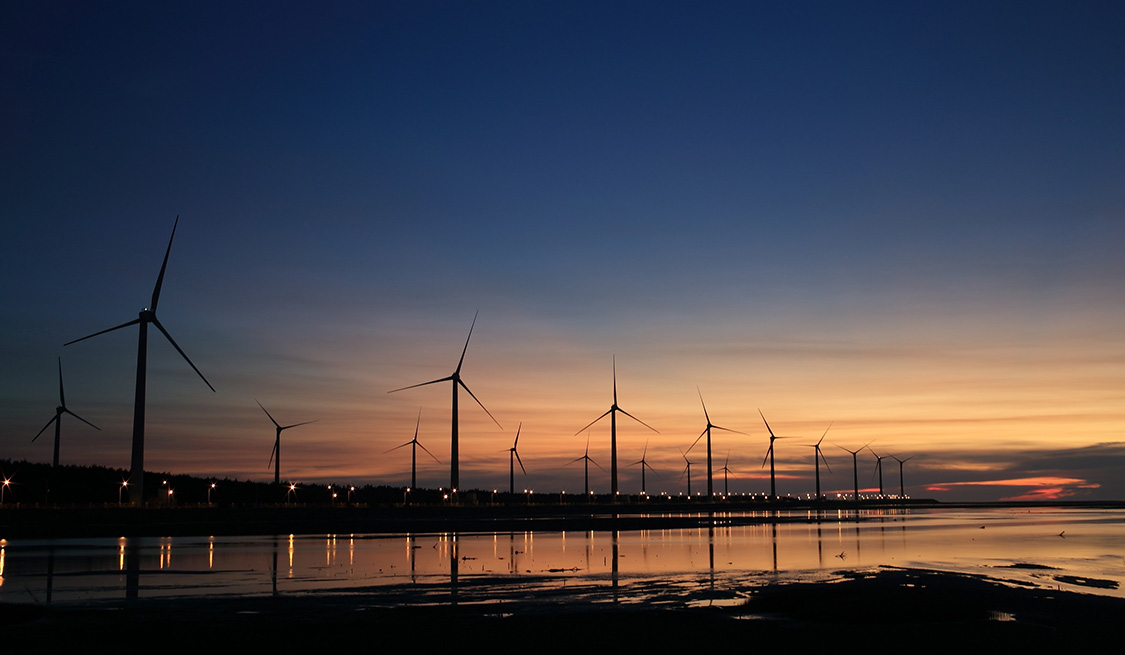Innogy Übernahme durch E.ON Blick vom Wasser: eine Vielzahl an Windrädern bei abendrotem Himmel.