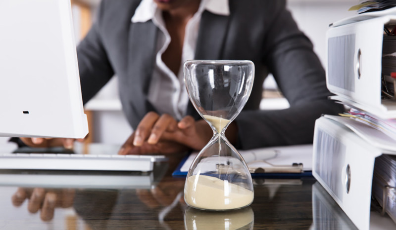 Wie lange hat der Stromanbieter Zeit für die Abrechnung? Frau im Büro am Schreibtisch sitzend. Neben Aktenordnern steht eine Sanduhr aus Glas