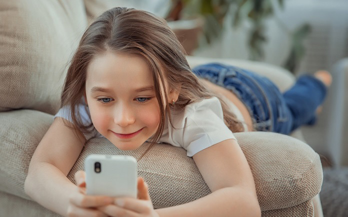 Mädchen liegt auf dem Sofa mit einem Smartphone in den Händen.