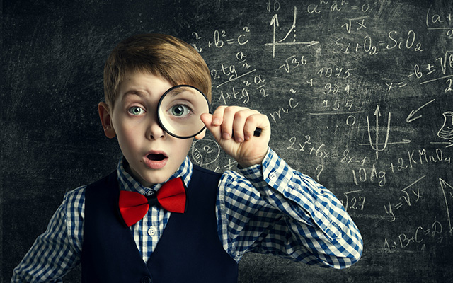 Kleiner Junge mit kariertem Hemd, Weste und roter Fliege hält sich eine Lupe vor das linke Auge. Hinter ihm eine Tafel mit mathematischen Formeln angeschrieben.