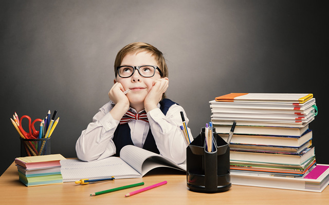 Kleiner Junge mit Brille, Hemd, Weste und Fliege sitzt am Schreibtisch. Den Kopf in die Hände gestützt und nach oben schauend. Neben ihm ein Stapel Bücher und Büro-Utensilien.