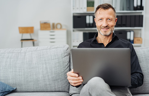 Mann sitzt auf dem Sofa mit Laptop auf dem Schoß.