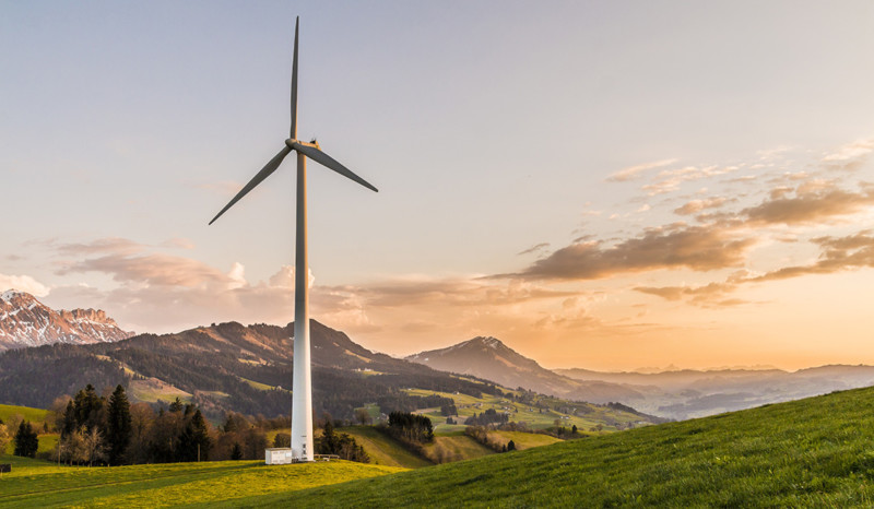 Energieverbrauch senken Windmühle auf einer Wiesenlandschaft. Im Hintergrund ein Gebirge und abendroter Himmel