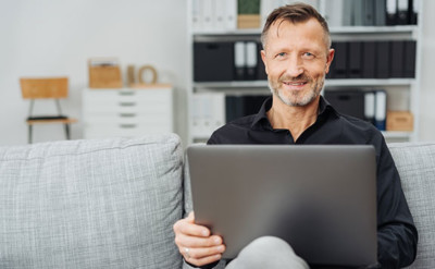 Kostenloses Angebot Mann sitzt auf dem Sofa mit Laptop auf dem Schoß.
