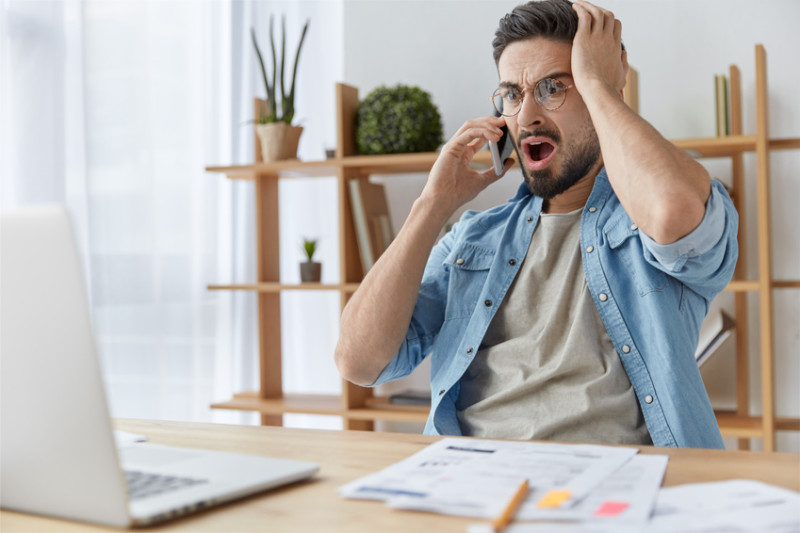 Innogy Preiserhöhung Mann mit Bart und Brille schaut entsetzt auf seinen Laptop, während er telefoniert. Sein Stromanbieter hat die Preise erhöht