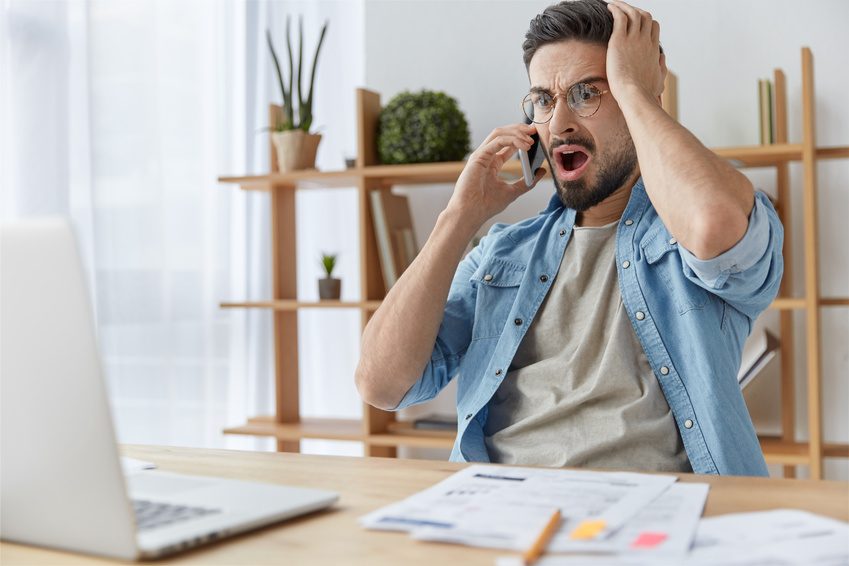 Innogy Preiserhöhung Mann mit Bart und Brille schaut entsetzt auf seinen Laptop, während er telefoniert. Sein Stromanbieter hat die Preise erhöht